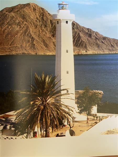 Faro blanco frente al mar y las montañas de San Felipe, con palmeras en primer plano