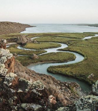 Humedales y canales de agua de San Quintín, con rocas en primer plano y la bahía al fondo